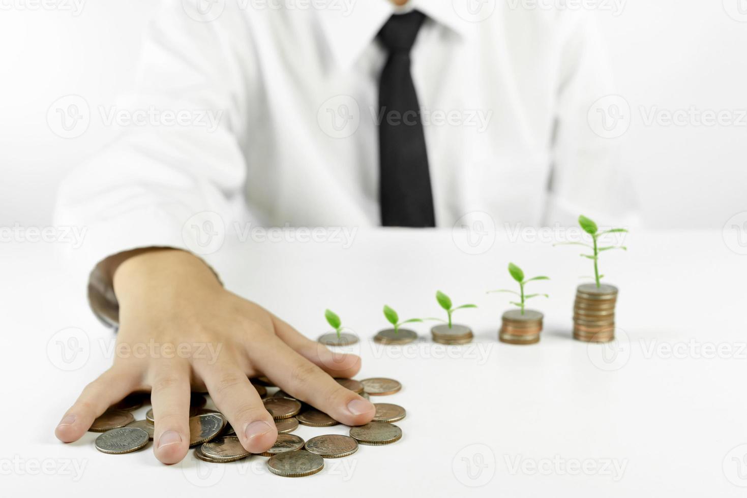 empresário segurando moedas com pilhas de árvores e moedas em fundo branco foto