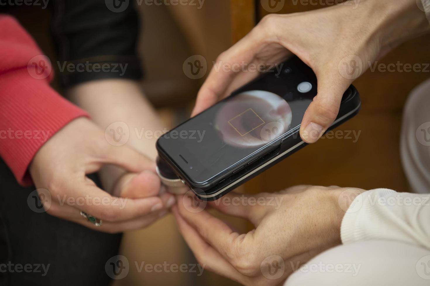 um dermatologista examina marcas de nascença e verrugas na perna do paciente. feche a imagem recortada do exame de marca de nascença com dispositivo moderno usando luz, aplicativo de telefone e câmera foto