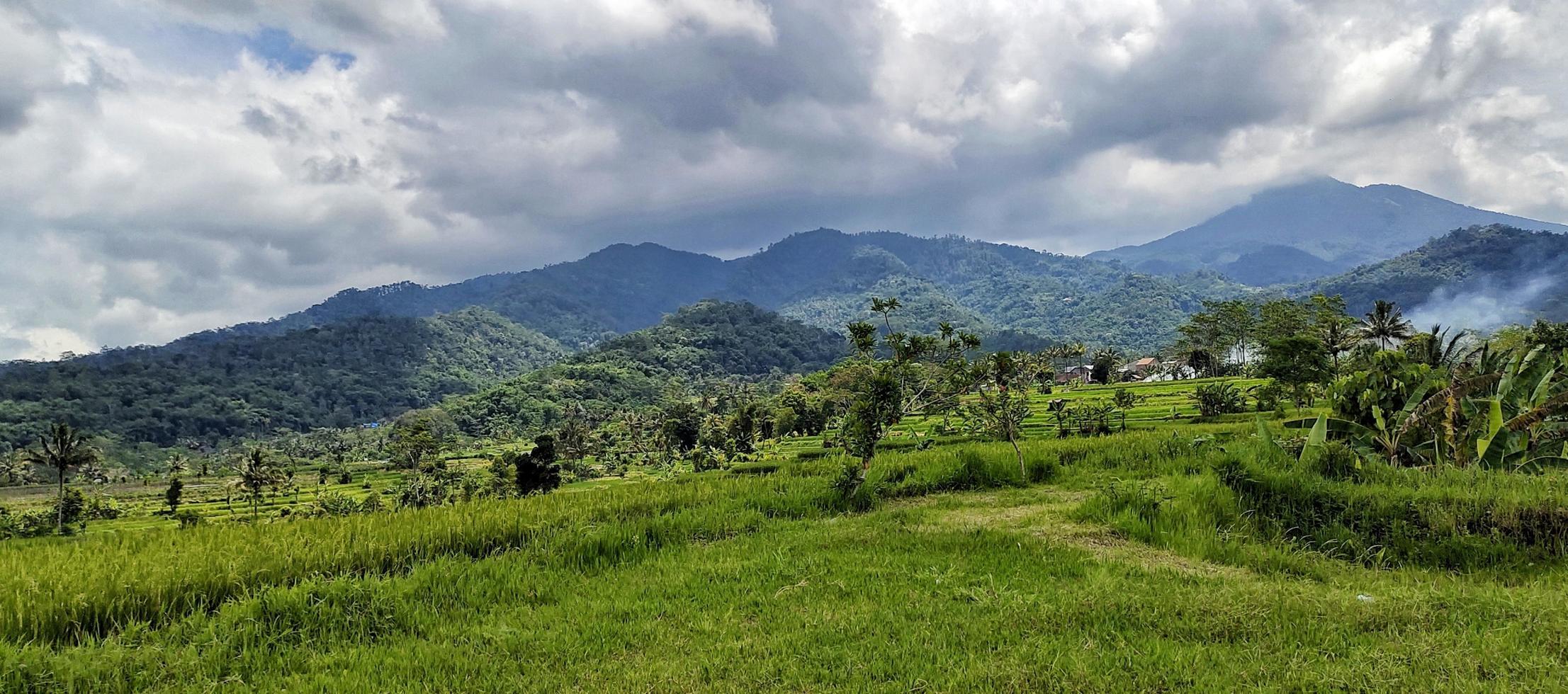 bela paisagem montanhosa com nuvens aglomeradas acima dela. vila rural em um vale de montanha na indonésia. vista da montanha. floresta tropical. fundo da natureza. foto