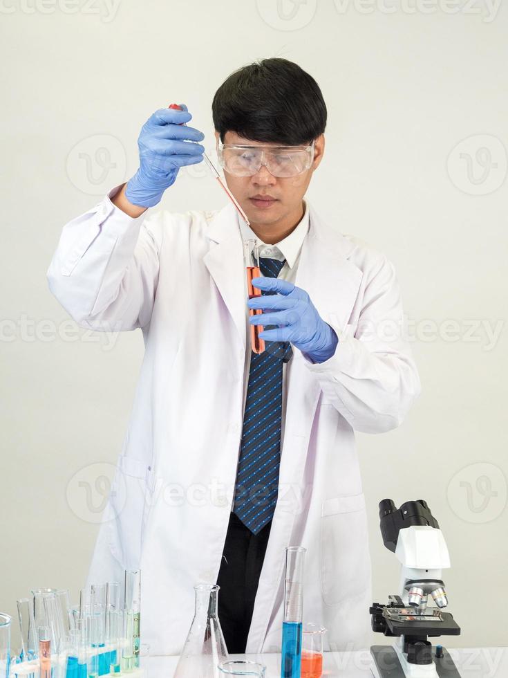 cientista estudante asiático no laboratório de mistura de reagentes em um laboratório de pesquisa científica com tubos de ensaio de vários tamanhos e microscópios. em cima da mesa no fundo branco do laboratório de química de laboratório. foto