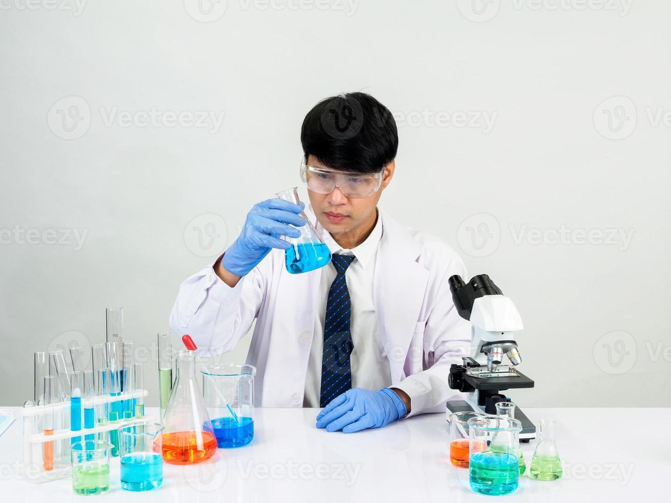 cientista estudante asiático no laboratório de mistura de reagentes em um laboratório de pesquisa científica com tubos de ensaio de vários tamanhos e microscópios. em cima da mesa no fundo branco do laboratório de química de laboratório. foto