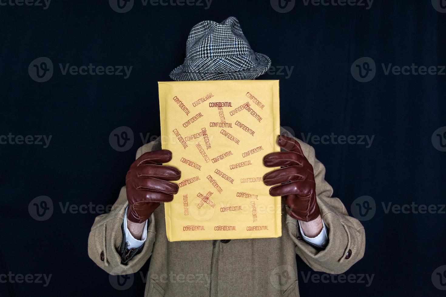 retrato de homem de casaco e chapéu segurando envelope confidencial sobre o rosto em fundo preto. filme noir agente secreto espião. roubo de identidade e crime. estilo retrô e moda vintage foto