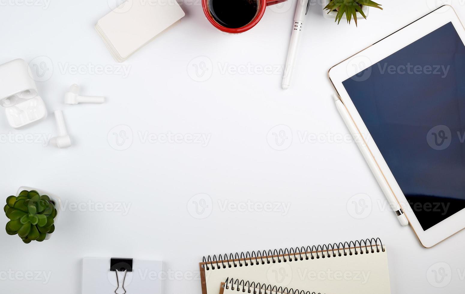 mesa branca com tablet eletrônico, cartões de visita em branco, xícara de café e fones de ouvido sem fio foto