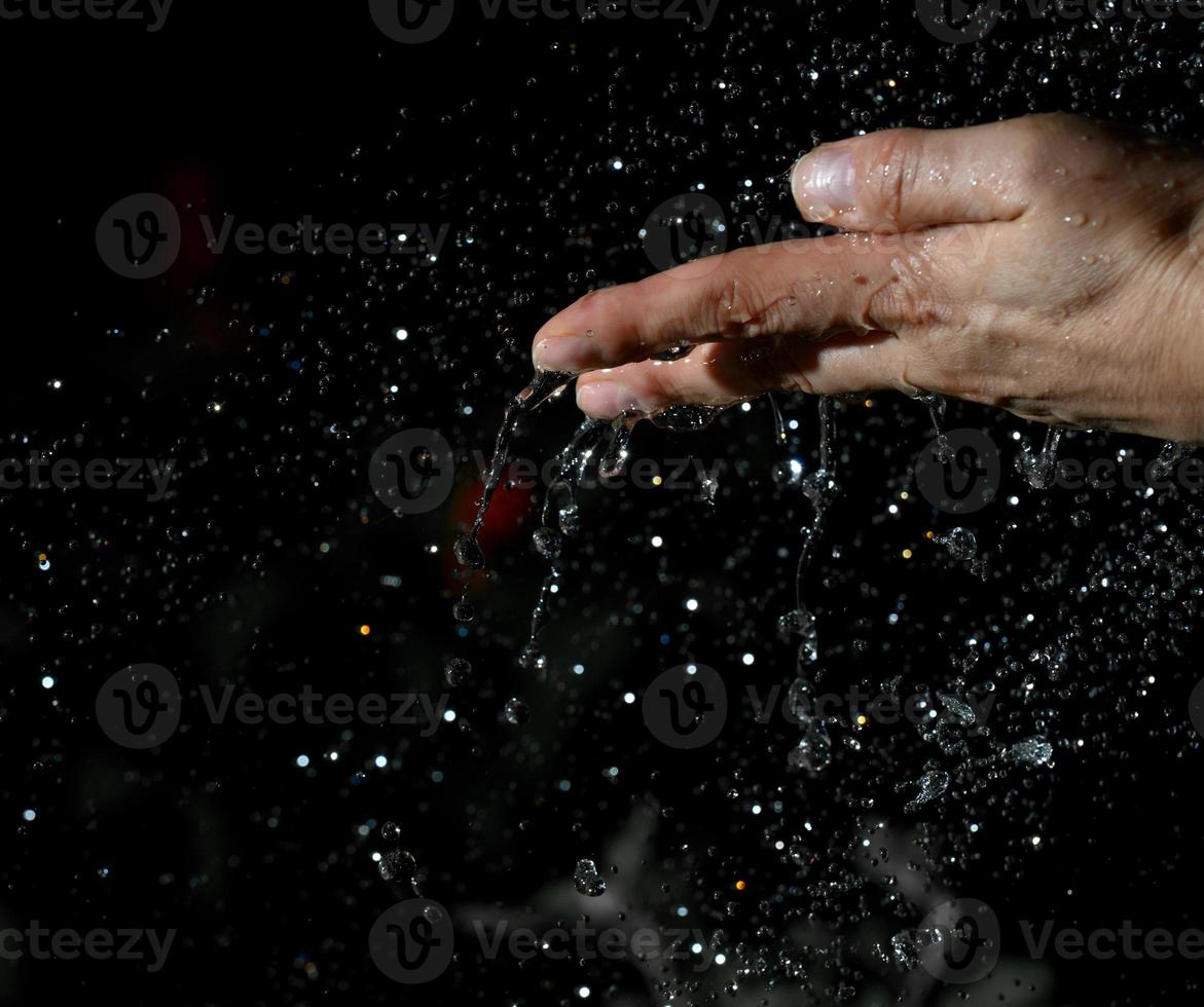 mão feminina e gotas de água voando sobre um fundo preto foto