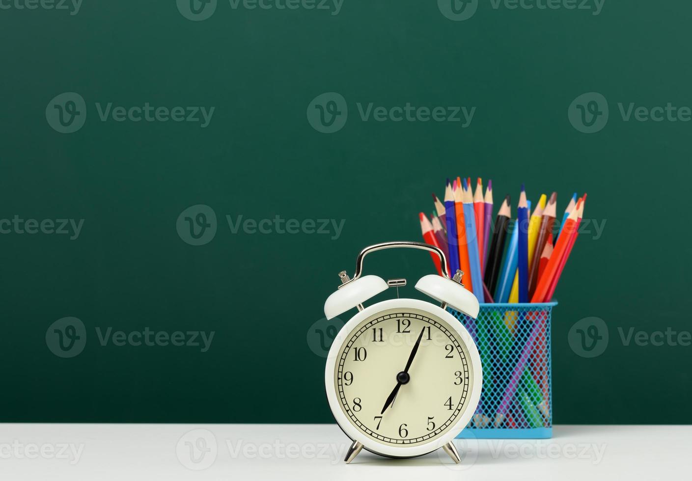 despertador redondo e lápis multicoloridos no fundo de um quadro de giz verde vazio. de volta à escola foto
