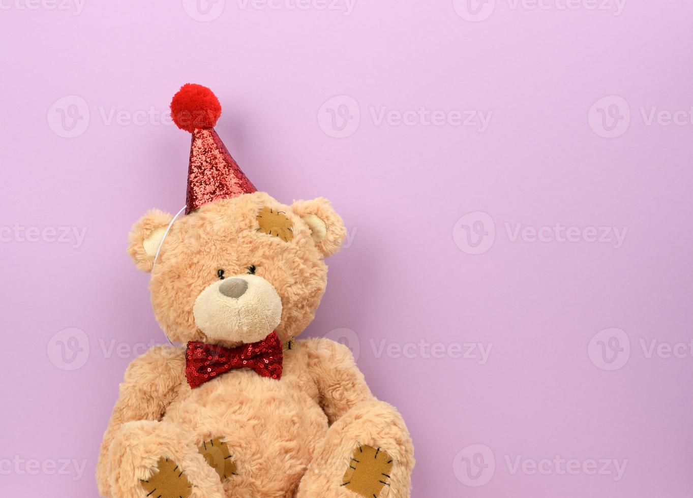 ursinho de pelúcia bege em um boné vermelho senta-se em um fundo roxo foto