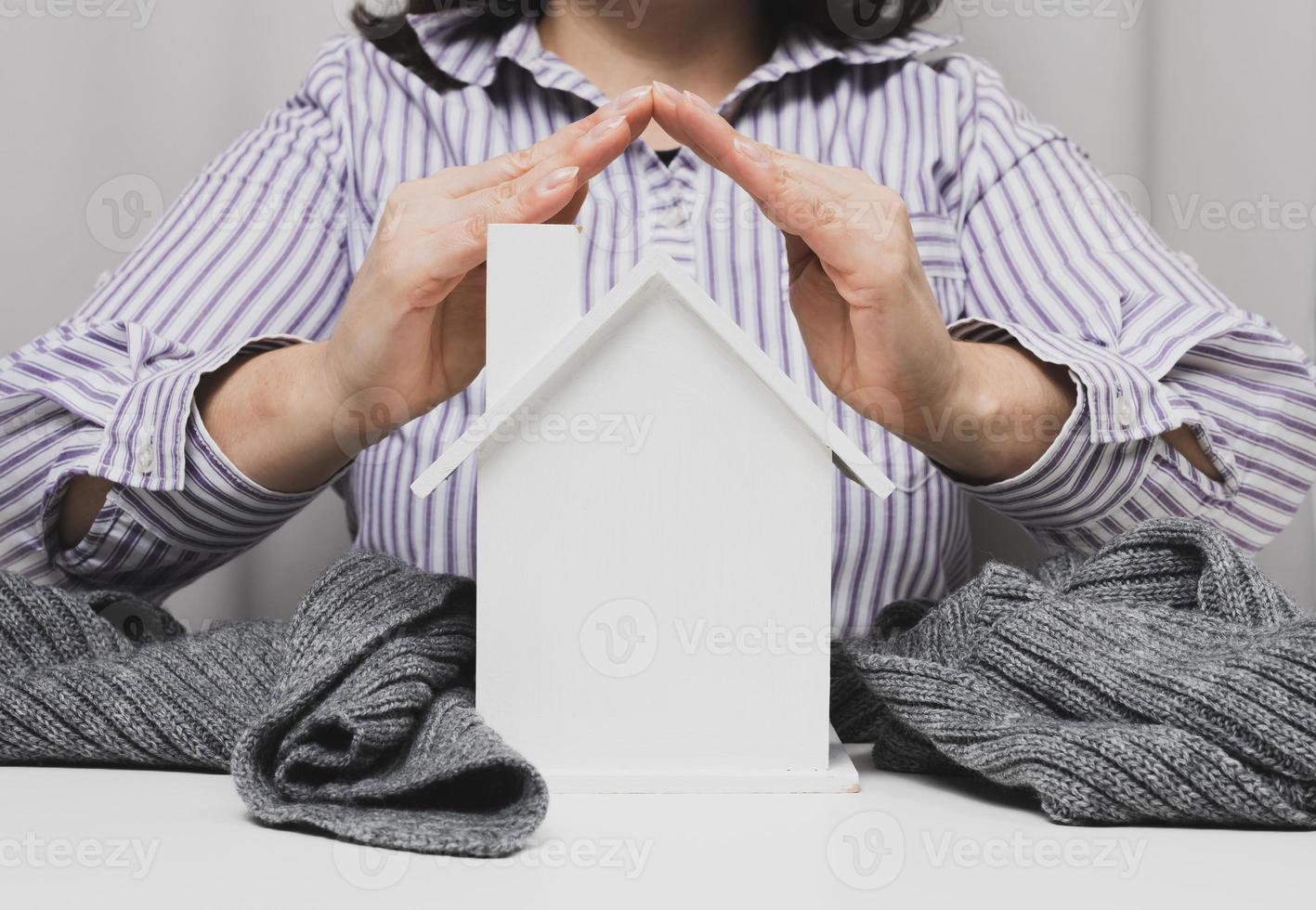 mãos femininas dobradas umas às outras sobre uma casa modelo em miniatura de madeira em um fundo branco. conceito de seguro imobiliário, proteção ambiental, felicidade familiar foto