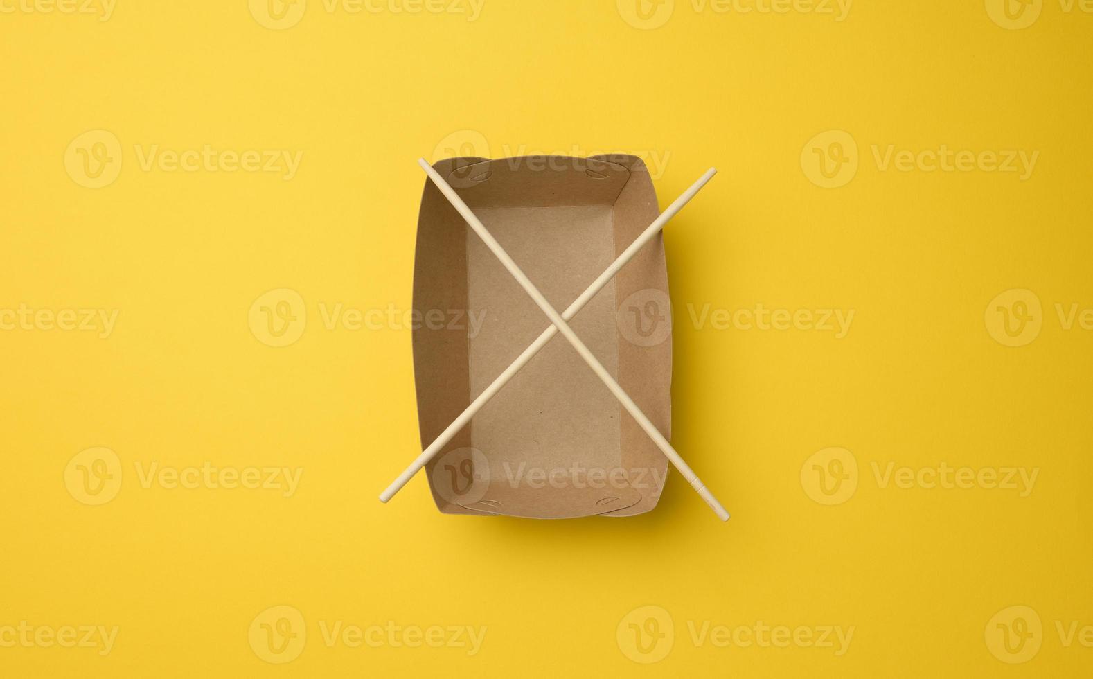 prato de papel pardo vazio e pauzinhos de madeira em um fundo amarelo, vista superior foto