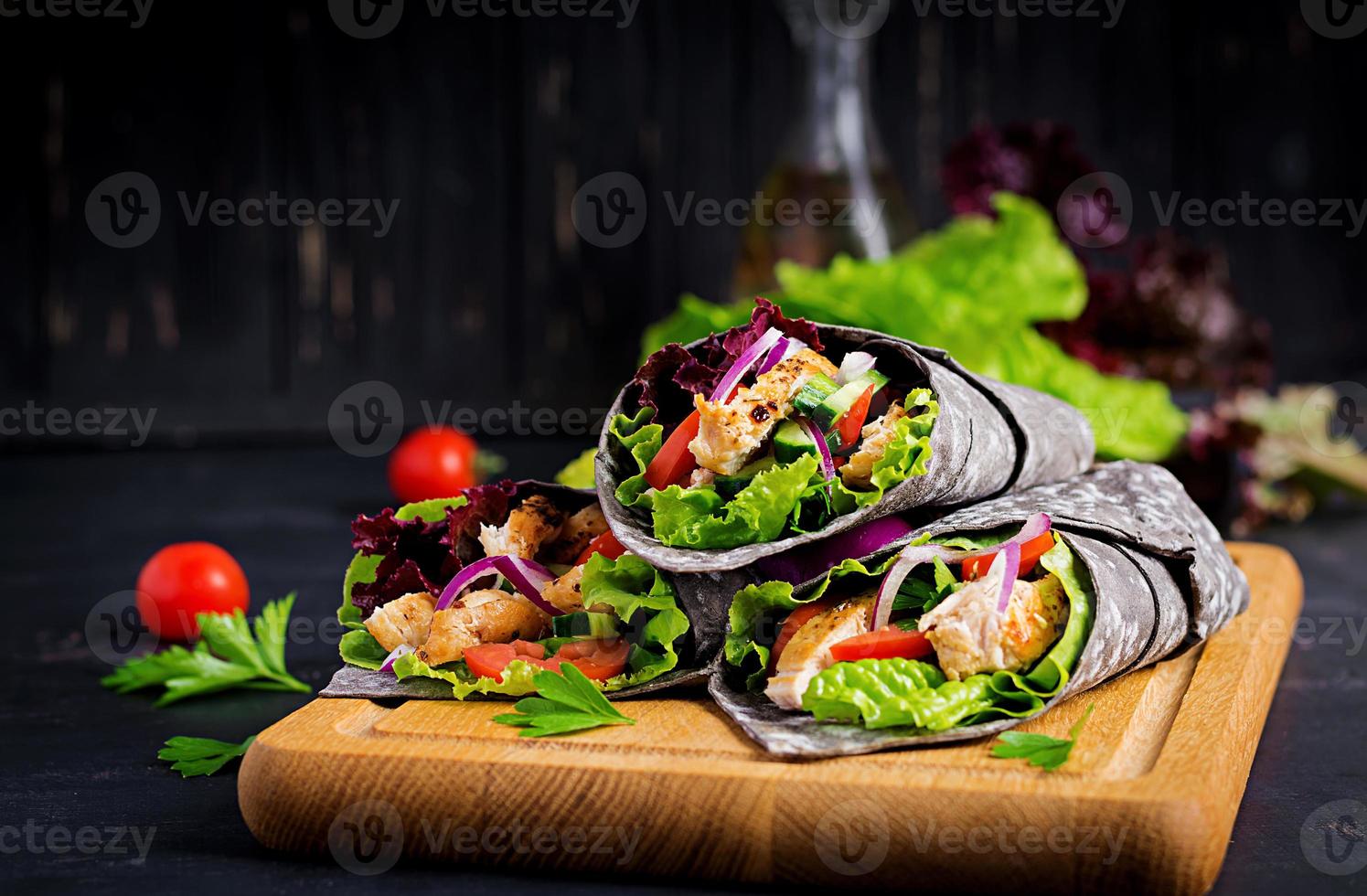 tortilla com choco adicionado de tinta envolve com frango e legumes em fundo preto. burrito de frango, comida mexicana. foto