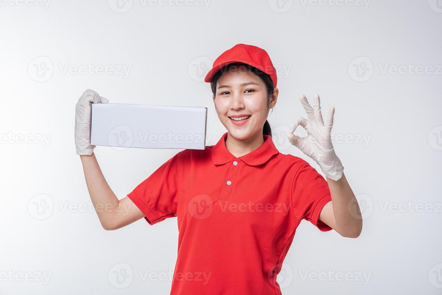 imagem do jovem entregador em uniforme de camiseta em branco de boné vermelho em pé com caixa de papelão branca vazia isolada no estúdio de fundo cinza claro foto