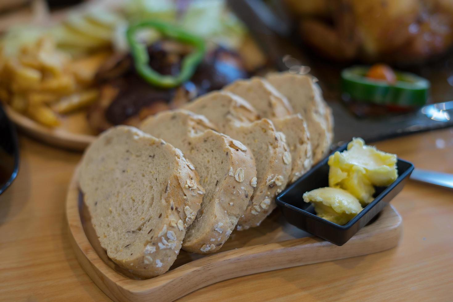 Pão fatiado com manteiga em prato de madeira foto