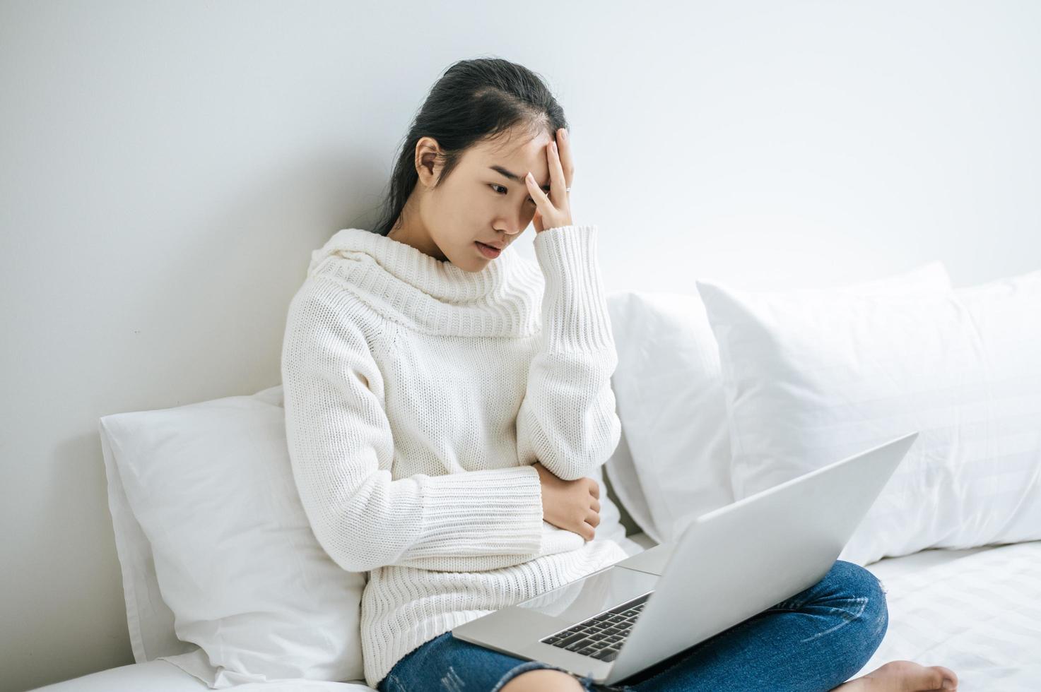 uma mulher sentada na cama brincando em seu laptop e sentindo estresse foto