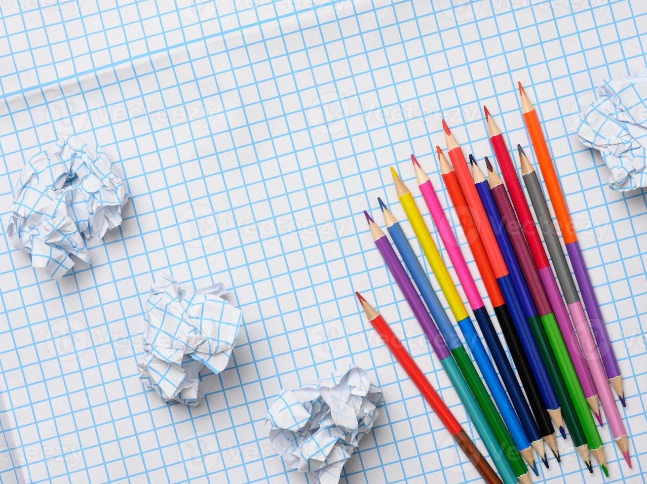 lápis de madeira multicoloridos e folhas de papel amassadas em fundo de papel quadrado branco foto