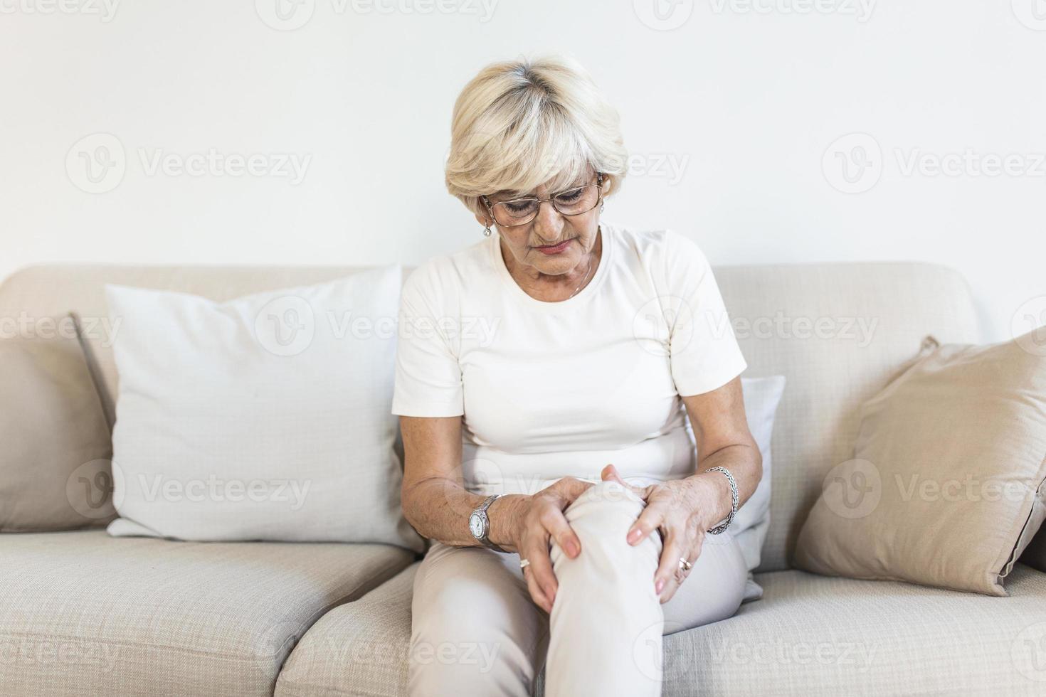 mulher sênior segurando o joelho com dor. velhice, problema de saúde e conceito de pessoas - mulher idosa que sofre de dor na perna em casa. mulher idosa que sofre de dor no joelho em casa foto