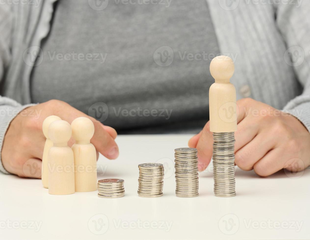 pilha de moedas de metal e figuras de madeira de homens em uma mesa branca. poupanças e despesas, orçamento familiar, subsídios do estado foto