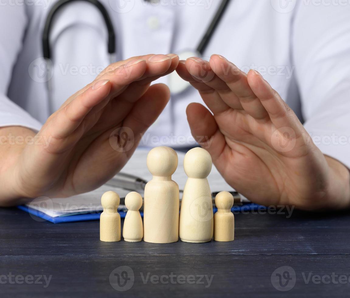 de madeira figuras do pequeno homens - uma família, a médico mãos cobrir a família para proteção a partir de doenças. saúde seguro conceito foto