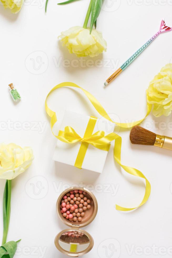 Maquiagem produtos com amarelo tulipa flores e uma presente caixa com uma arco em uma branco fundo foto