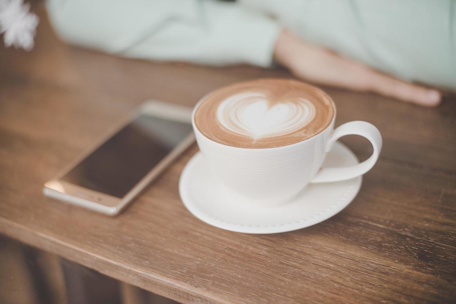 a mão do homem com uma xícara de café latte art e smartphone no café bar foto