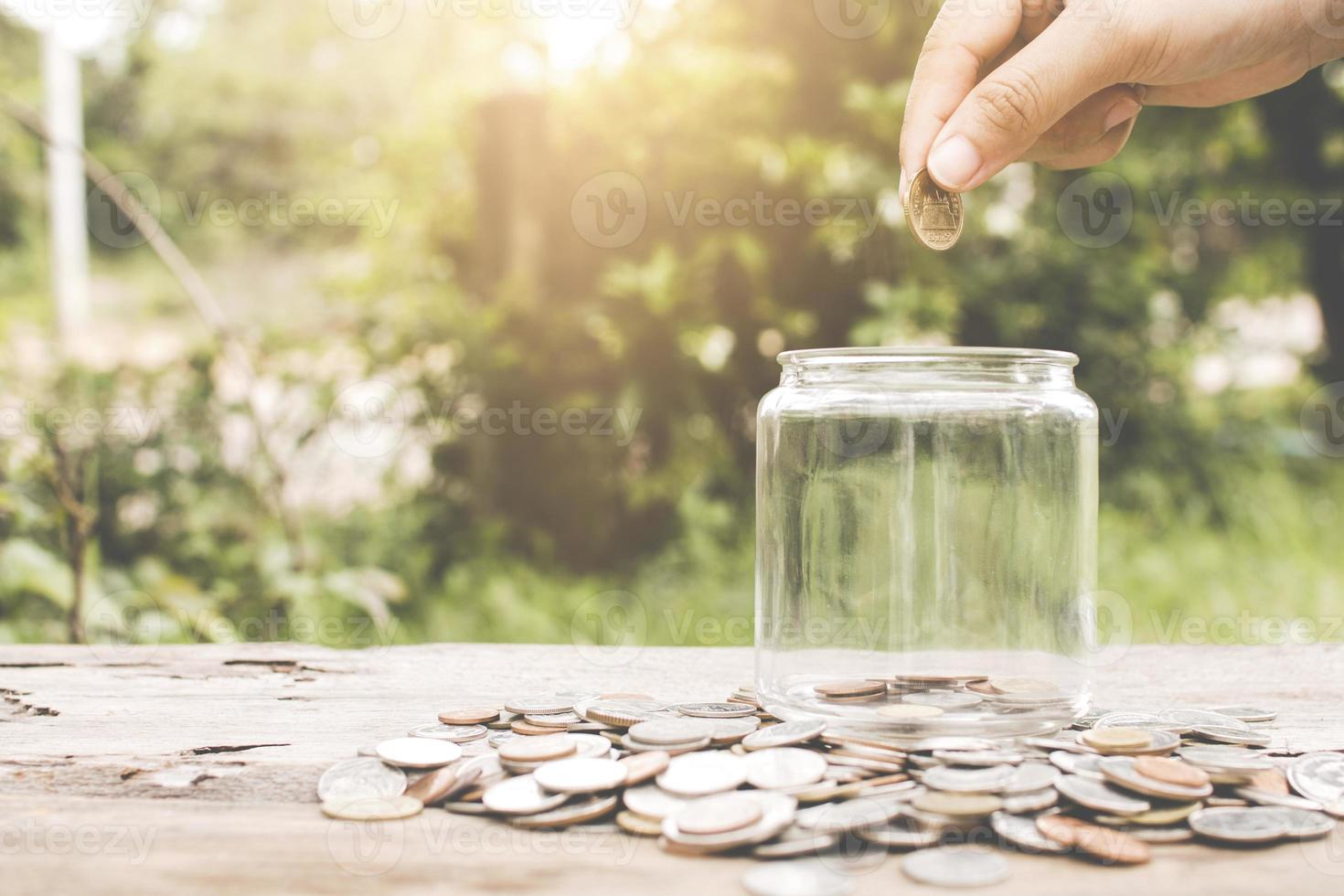 mão colocando dinheiro em pote de vidro foto