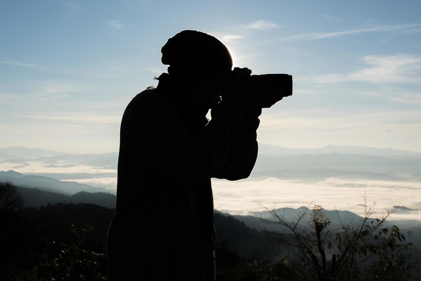 silhueta de jovem fotógrafo segurando uma câmera com paisagem de montanha foto