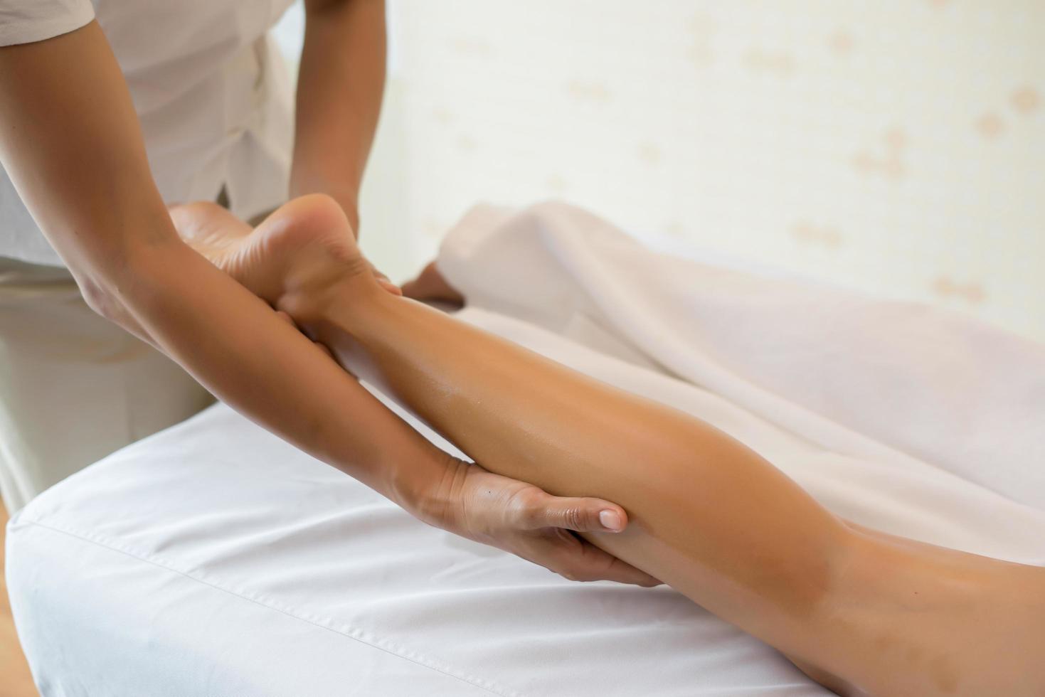 close-up de massoterapeuta massageando perna feminina em salão de spa foto