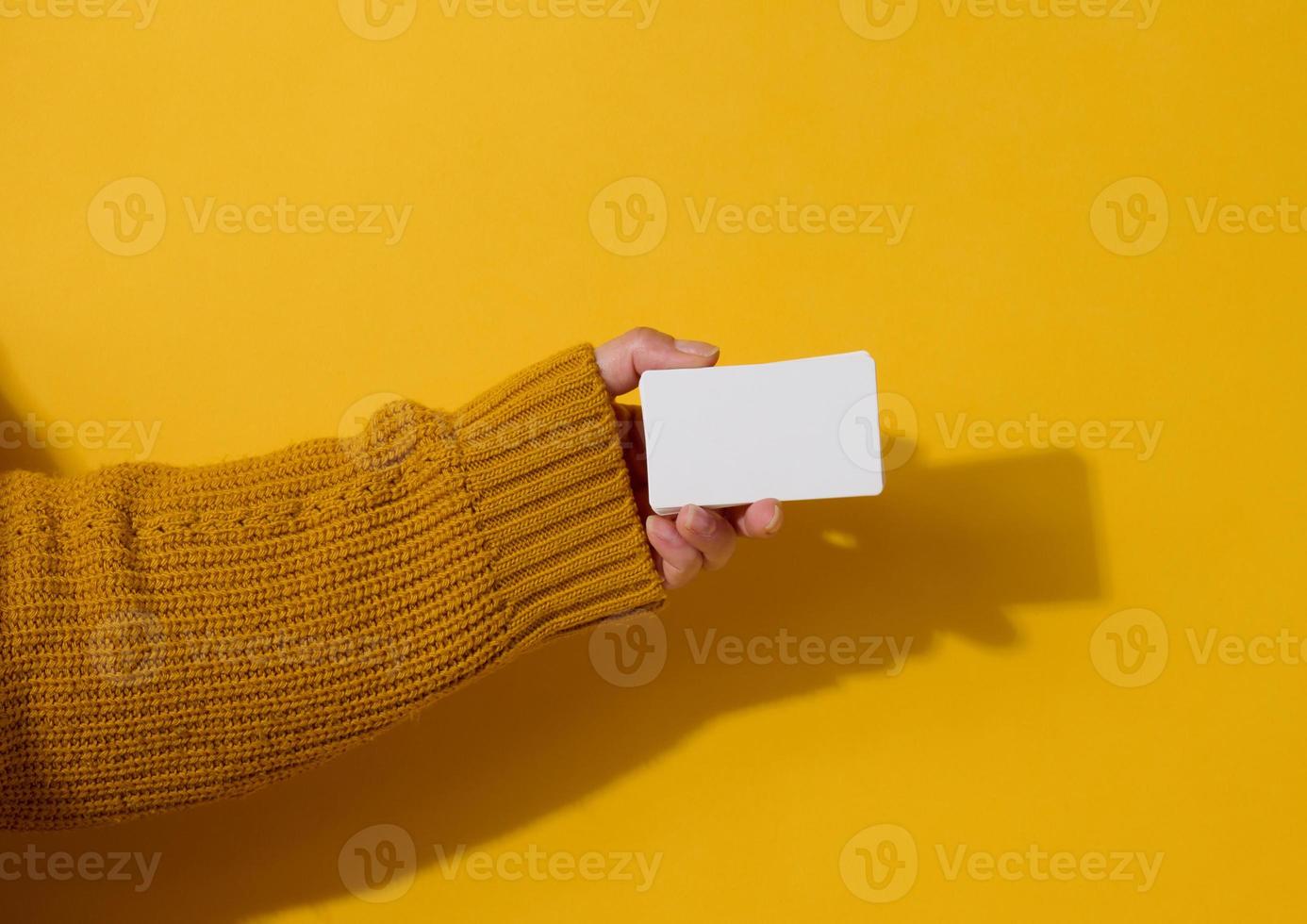 fêmea mão segurando esvaziar papel branco o negócio cartão em uma amarelo fundo. cópia de espaço foto