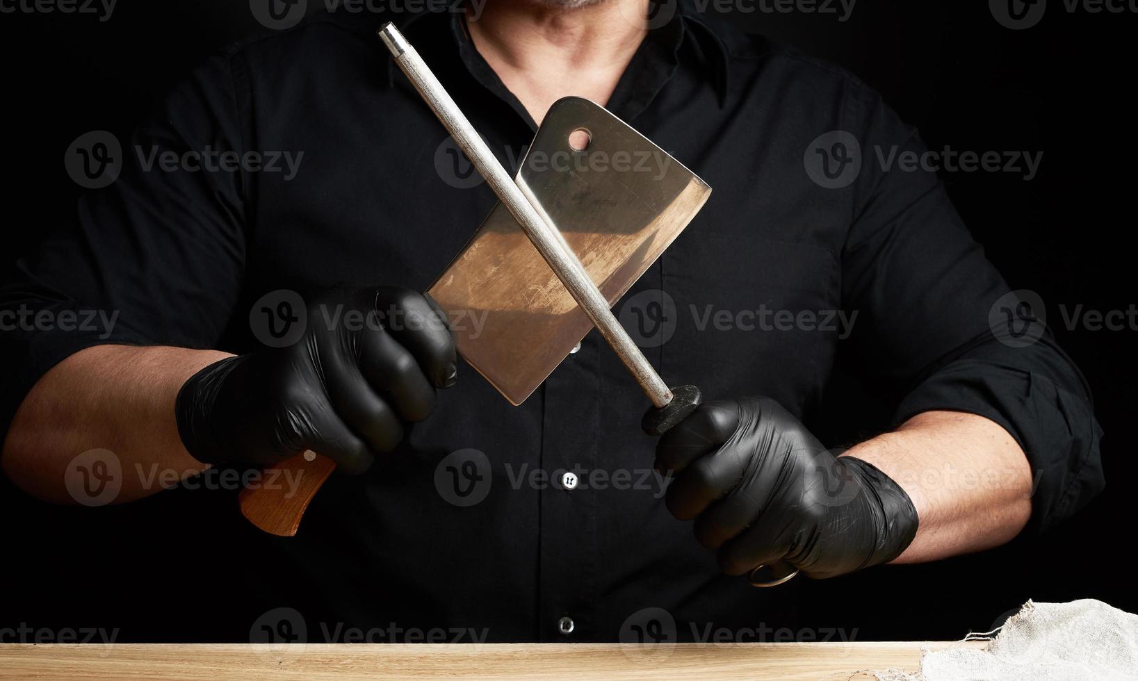 chefe de cozinha dentro uma Preto camisa e Preto látex luvas aguçar uma cozinha faca em a ferro apontador com uma lidar com foto