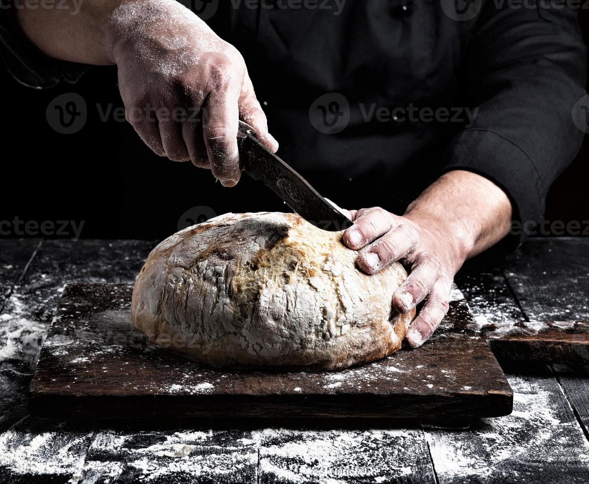 homem cortes com uma faca uma volta todo pão do branco trigo farinha foto