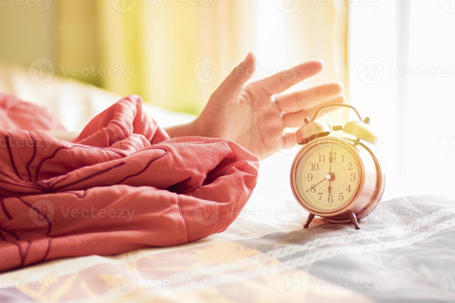 mão parando o despertador na cama às 6 horas foto