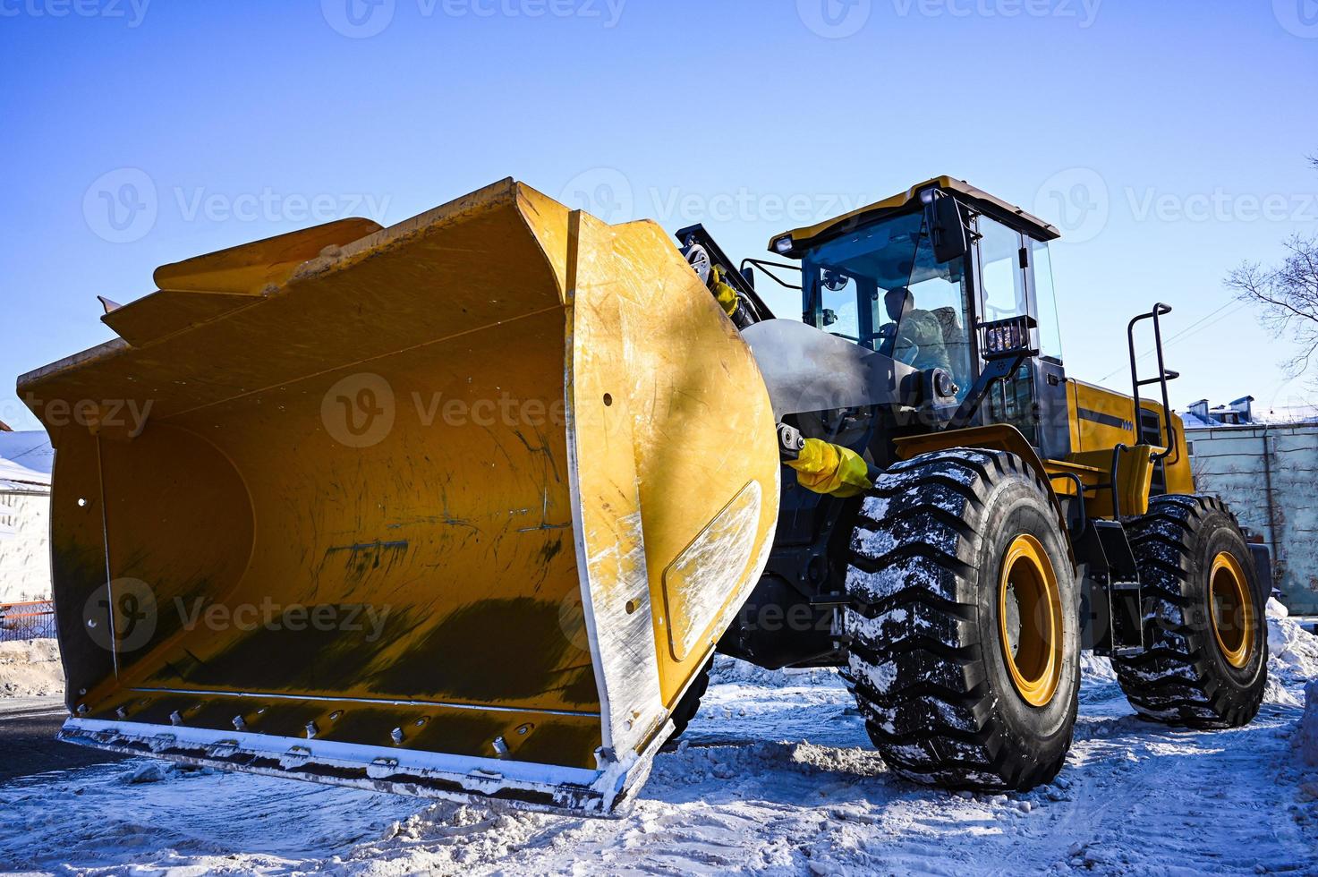 retroescavadeira carregador em a estrada. uma amarelo trator remove neve em a rua. foto