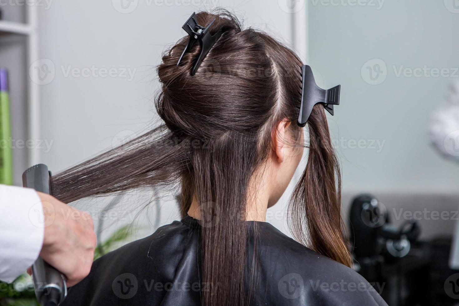 cabeleireiro aplica uma máscara de cabelo em cabelos pretos lisos. cuidados com os cabelos no salão de beleza. foto