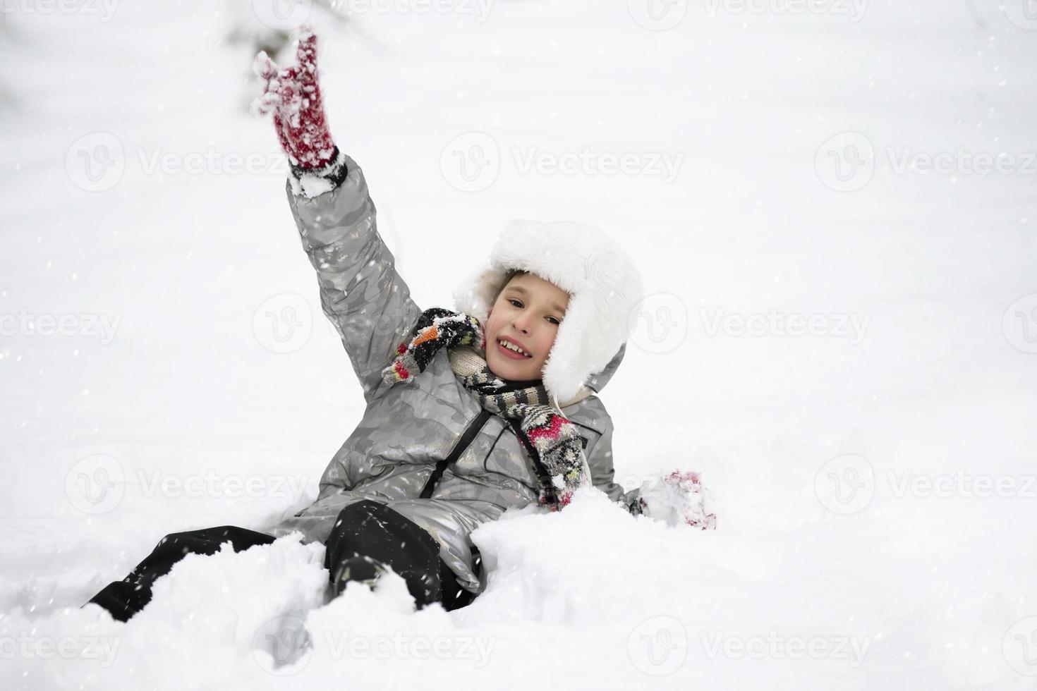 uma alegre Garoto dentro caloroso roupas mentiras dentro a neve. criança em uma inverno andar. foto