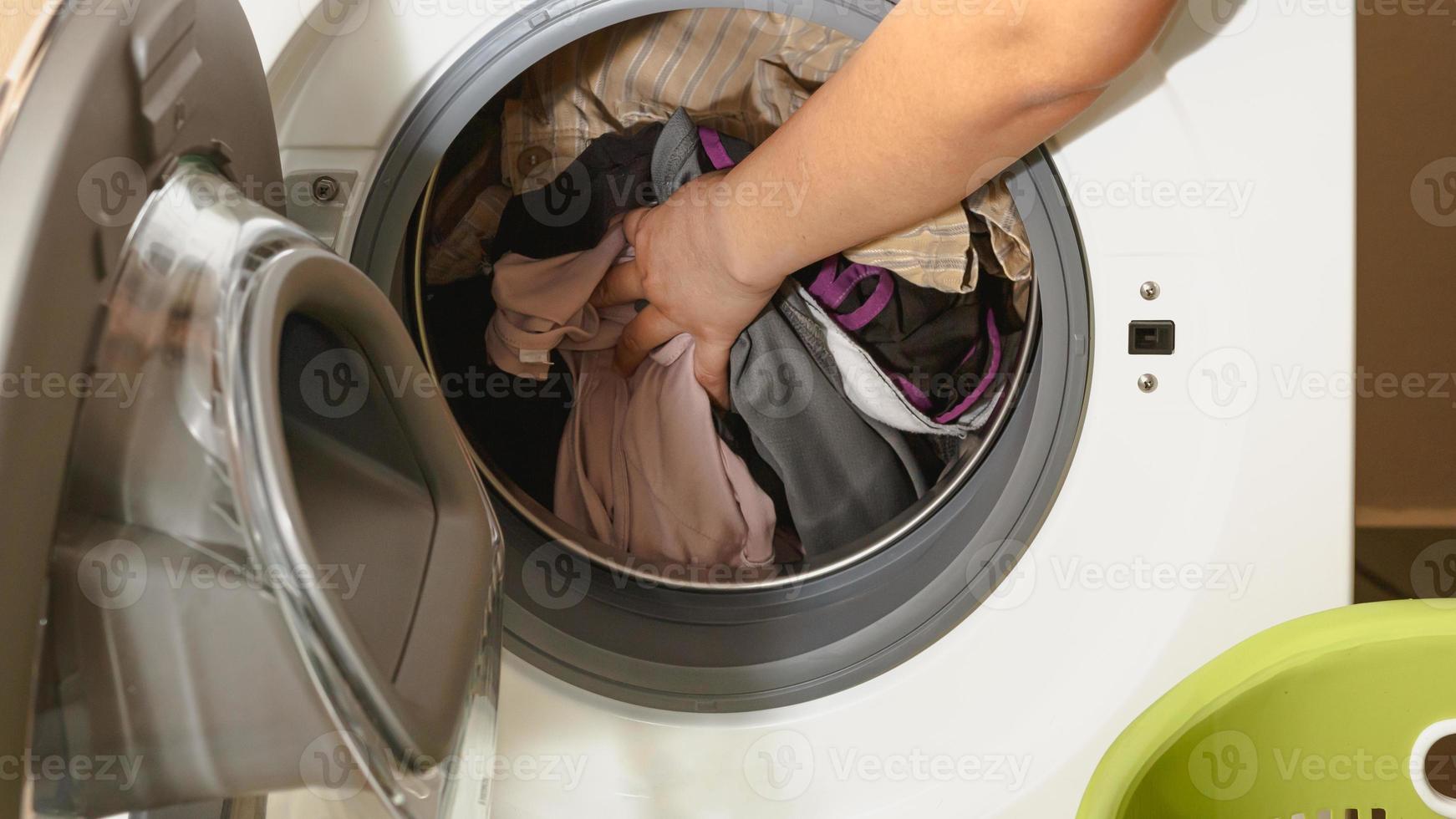 close-up da mão de uma mulher colocando roupas sujas na máquina de lavar. foto
