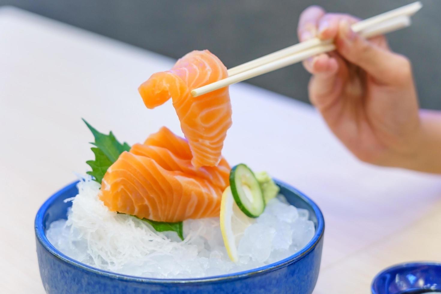 mão segurando sashimi de salmão usando pauzinhos foto