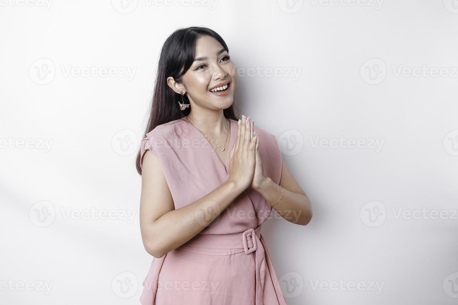 sorridente jovem ásia mulher vestido dentro rosa, gesticulando tradicional cumprimento isolado sobre branco fundo foto