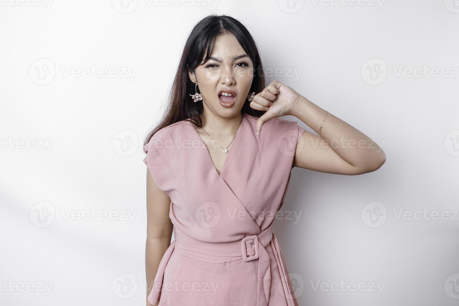desapontado ásia mulher vestindo Rosa blusa dá polegares baixa mão gesto do desaprovação, isolado de branco fundo foto