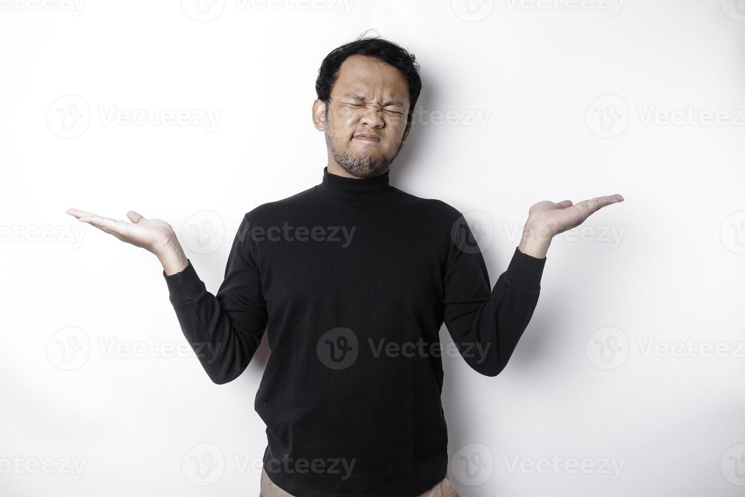 uma retrato do a ásia homem vestindo uma Preto camisa parece tão confuso entre escolhas, isolado de uma branco fundo foto