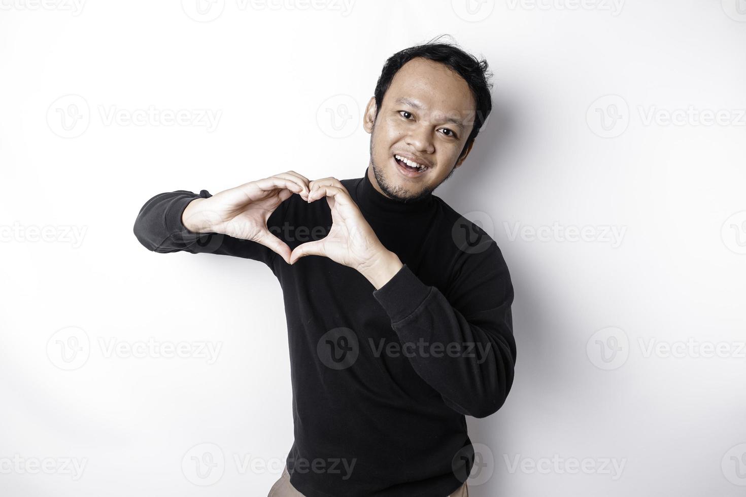 uma feliz jovem ásia homem vestindo uma Preto camisa sente romântico formas coração gesto expressando concurso sentimentos foto