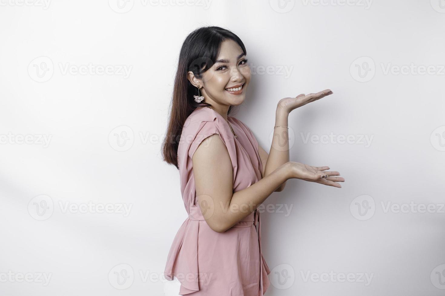 animado ásia mulher vestido dentro rosa, apontando às a cópia de espaço ao lado dela, isolado de branco fundo foto