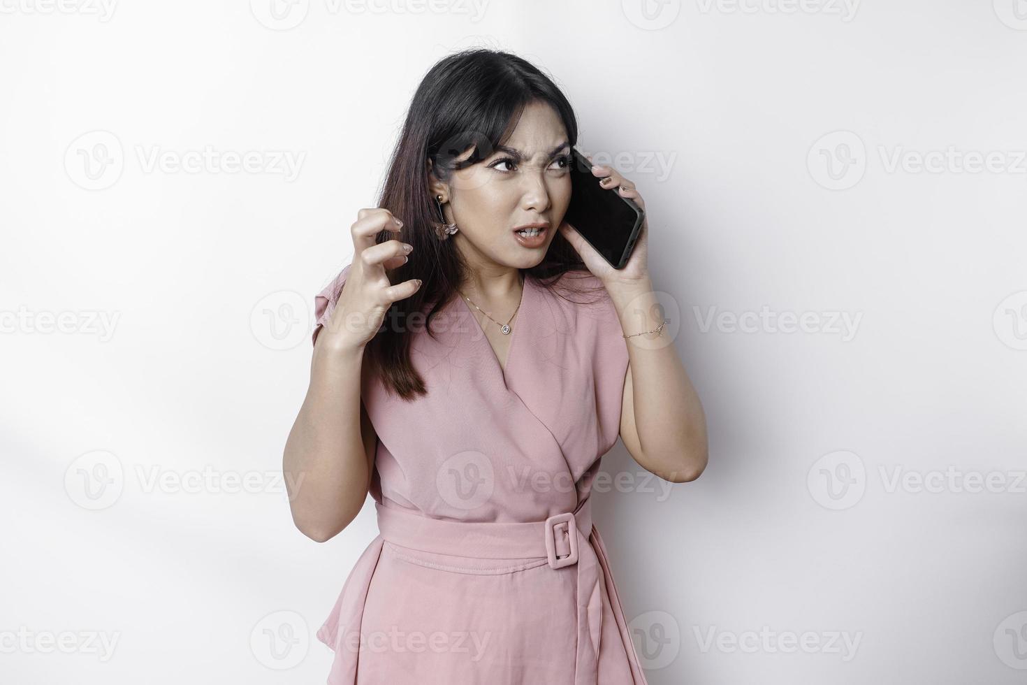 uma insatisfeito jovem ásia mulher vestido dentro rosa, parece desapontado com irritado face expressões segurando dela telefone foto