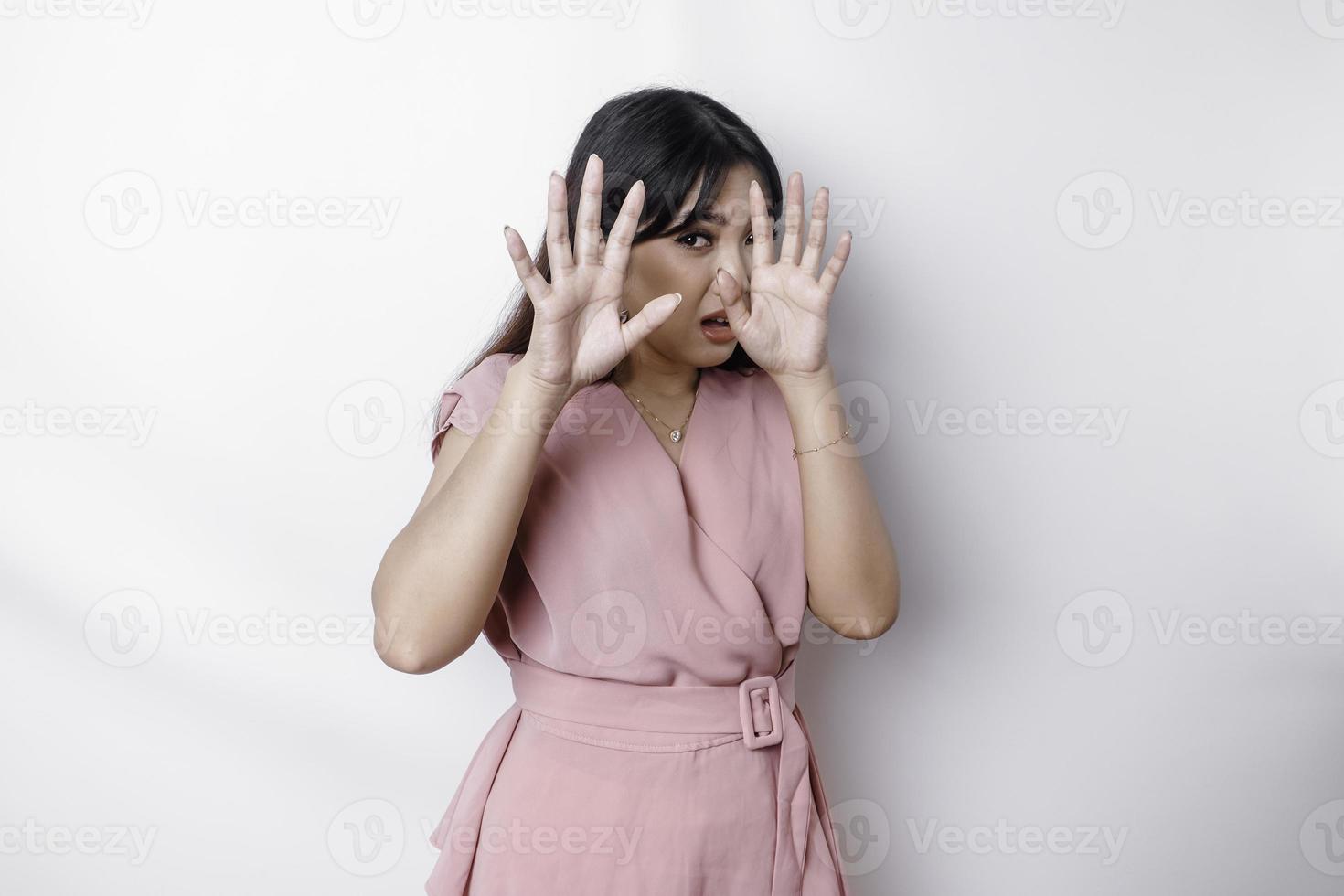 jovem mulher asiática isolada no fundo branco, parece deprimida, rosto coberto por dedos assustados e nervosos. foto