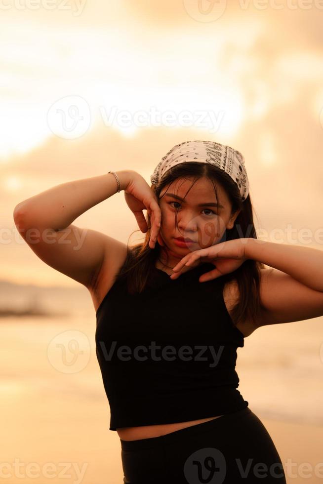 a ásia adolescente vestindo uma branco bandana e Preto camisa com uma sexy expressão em a de praia areia foto