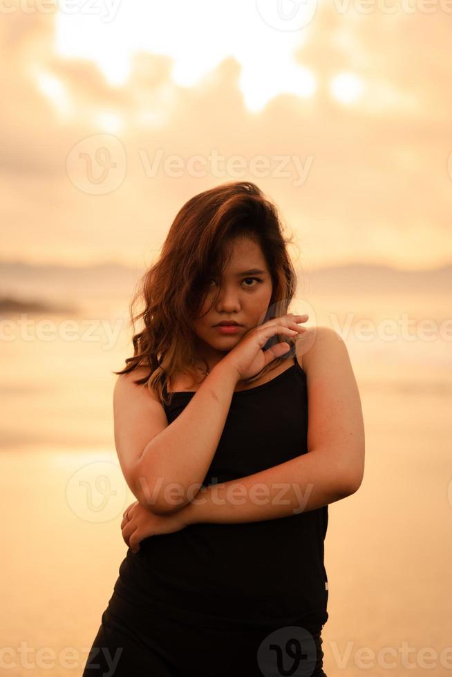 a ásia mulher dentro uma Preto vestir com uma muito sexy expressão atrai a atenção do pessoas por aí a de praia foto