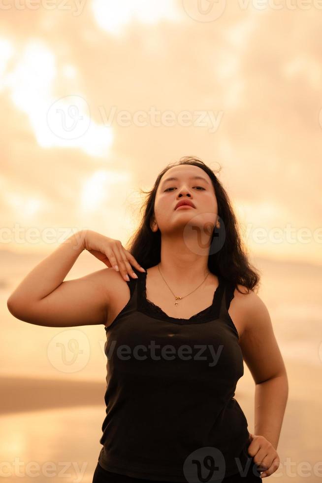 retrato imagem do a ásia mulher com Preto cabelo e a Bravo expressão em pé em a de praia dentro dela Preto roupas foto