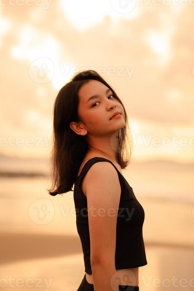 uma lindo ásia mulher dentro Preto roupas é desfrutando a beleza do a de praia com uma sorridente expressão em dela face enquanto em período de férias foto