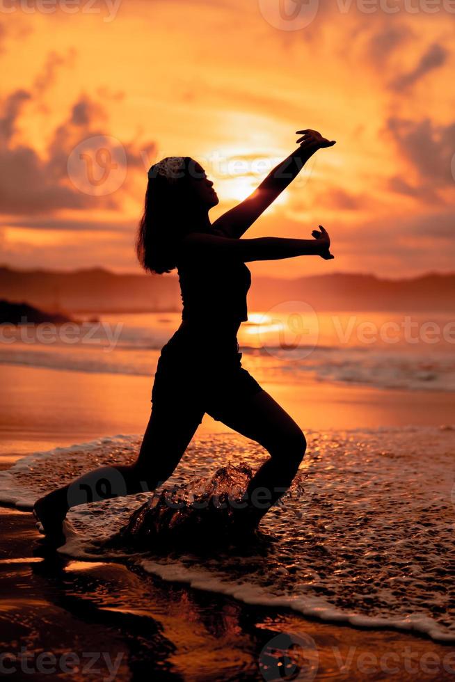 a silhueta do a ásia adolescente dentro Preto roupas posando com dela corpo acima a beira-mar ondas muito belas foto