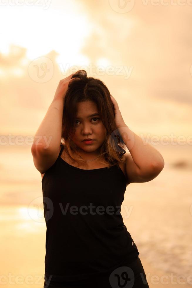 a ásia mulher com Castanho cabelo e Preto roupas faz sexy poses muito habilmente enquanto desfrutando a de praia foto