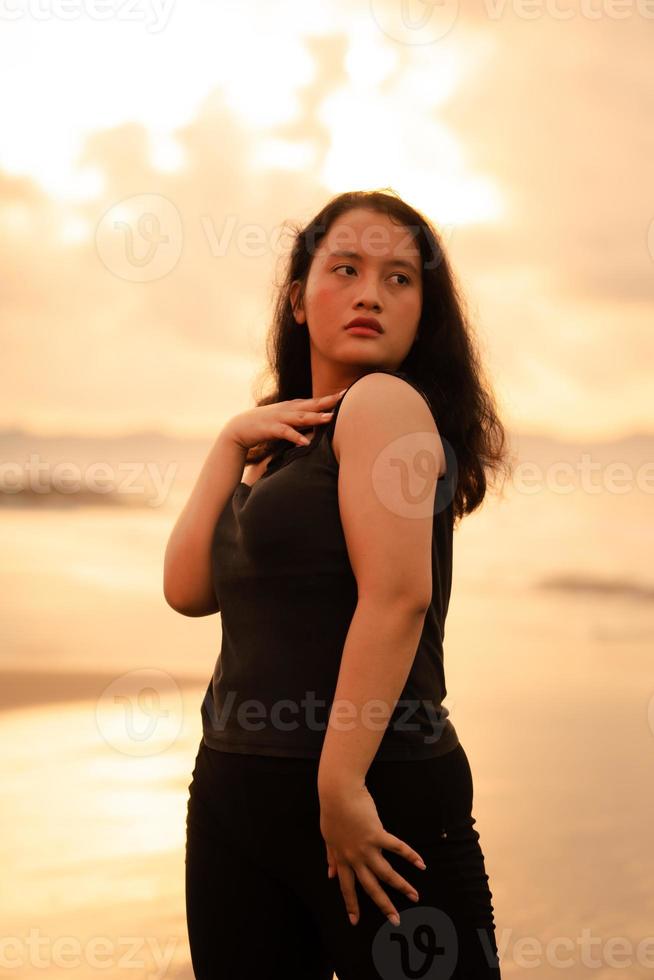 a ásia mulher posando com dela mãos elevado e tocante dela Preto cabelo apaixonadamente em a de praia foto