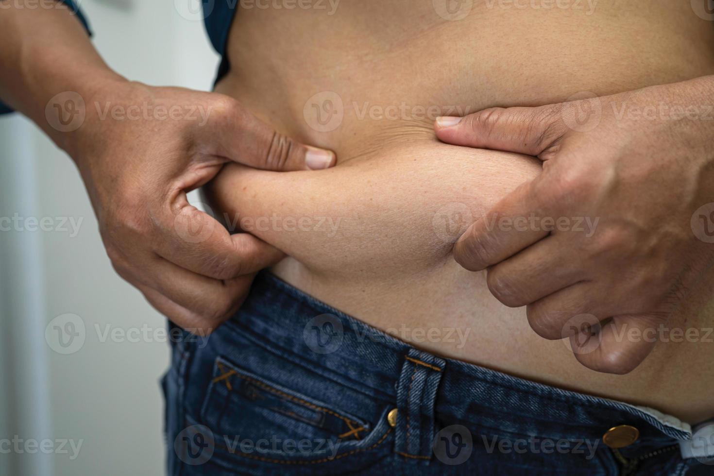 mulher asiática com excesso de peso mostra e usa a mão para apertar a barriga gorda. foto