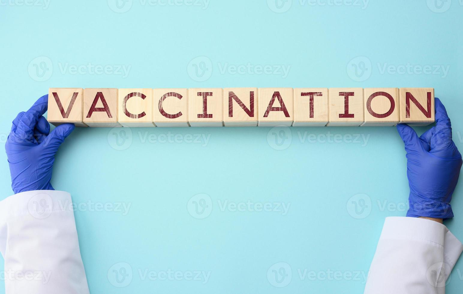 médico mãos dentro azul látex luvas aguarde cubos com a inscrição vacinação em uma azul fundo foto